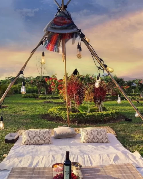 Picnic decorado con luces colgantes y vino en los jardines de Mundo Yanashpa, rodeado de vegetación tropical y un cielo al atardecer en Tarapoto.