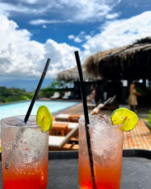 Dos cócteles refrescantes con rodajas de limón servidos junto a la piscina infinita de Mundo Yanashpa en Tarapoto, rodeados de naturaleza y un cielo despejado.